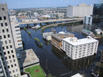 View from an upper level of Charity Hospital looking towards I-10/Claiborne Ave. Every street visible for miles is covered in floodwaters, some scattered debris is floating on the water. A few car roofs are visible submerged in the water. People can be seen standing or walking on the interstate and interstate ramps. by LSU Health Sciences Center - New Orleans
